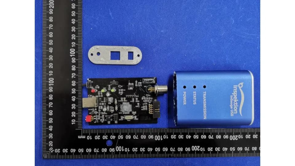 แผงวงจร InGauge USB วางข้างกล่องอะลูมิเนียมสีน้ำเงินและแผ่นปิดท้าย บนแผ่นไม้บรรทัดวัดขนาด